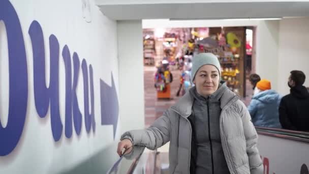 Uma mulher sorridente monta uma escada rolante numa loja. Centro comercial — Vídeo de Stock