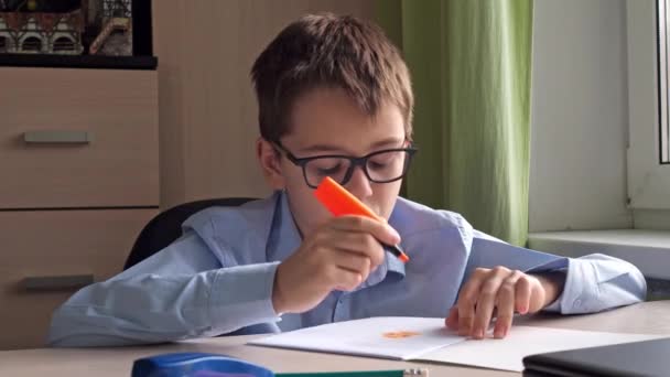 A teenager in a blue shirt draws in a notebook with a text guide. writing materials. a desk. home lessons — Vídeo de Stock