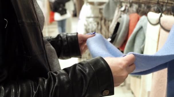 Las manos de las mujeres sienten la tela de la bufanda. Una mujer elige cosas en una tienda. una gran tienda de ropa — Vídeo de stock