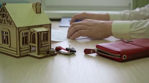 Человек подписывает контракт. есть деревянный дом на столе, ключи от дома — стоковое видео