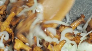 Mantarlı soğan kızartma tavasında kızartılır. Tahta bir spatulayla karıştırmak. yemek yapmak