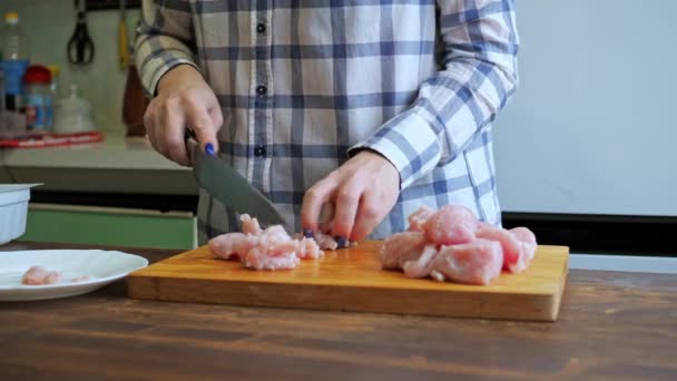Žena krájí kuřecí řízek na dřevěné desce. vaření v kuchyni. detailní záběr rukou s nožem a stolem — Stock video