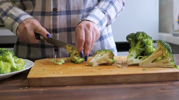 As mãos de mulheres cortam o brócolis em uma tábua de redução com uma faca. alimentação saudável. cozinhar — Vídeo de Stock