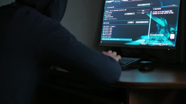 Человек в толстовке в капюшоне сидит за компьютером в темноте. свет от компьютера. Лицо не видно. программирование — стоковое видео