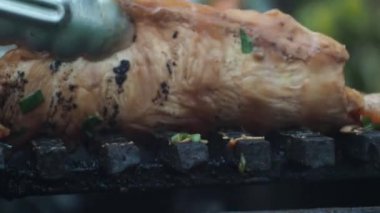 Izgarada tavuk filetosu pişirmek. Aşçı ızgaradaki fileto dilimlerini maşayla çevirir. Arka planda bir yangın yanıyor