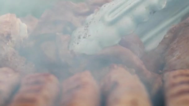 Szczypcami obraca uda kurczaka na grillu. w dymie z węgla — Wideo stockowe