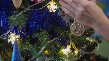 Bir Noel ağacını kardan adam oyuncağıyla süsleyen çocukların elleri parlak festival ışıklarının arka planında. Çocuklar Noel ağacını süslüyor.