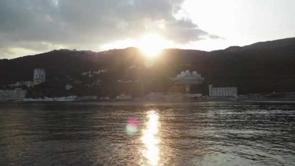 Sunset. view from the sea to the coastline. mountainous area with hotels near the water. the sun is peeking out from behind the mountains — Stockvideo