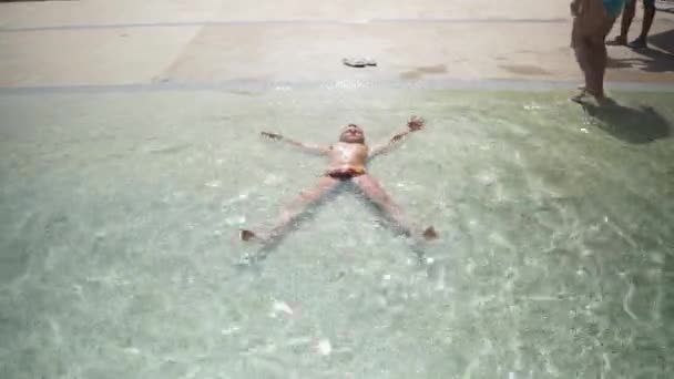 Tonåringen sträcker ut sina armar och ben som ligger i den grunda delen av poolen. En asterisk. koppla av i utomhuspoolen — Stockvideo