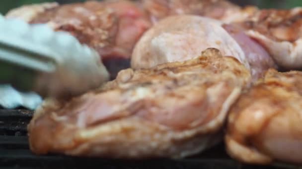 With tongs, he turns the chicken thighs on the grill. focus on the middle of the grid. they acquire a toasted color — Stock video