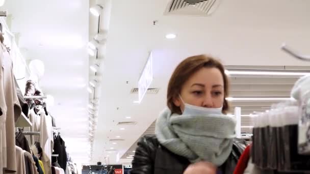 A woman chooses things in a store. a large clothing store. a woman in a mask — Vídeo de Stock