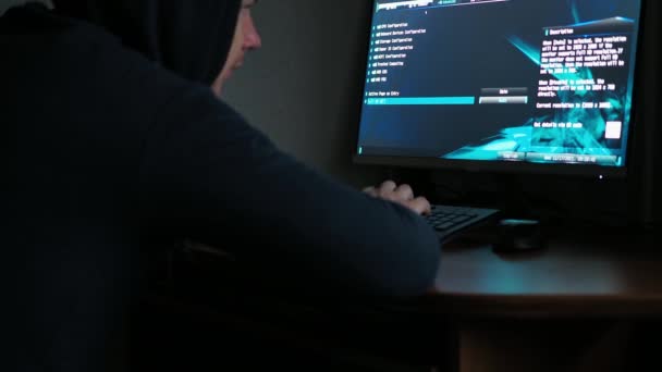 Kapüşonlu sweatshirt giyen bir bilgisayar korsanı karanlıkta bilgisayarın başında oturuyor. Bilgisayardan gelen ışık. klavyeden kod yazar — Stok video