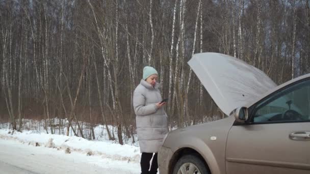 Hysterical laughter, a frozen woman is on the phone calling for help, a car broke down outside the city in winter. dangerous frost. traffic situation. calling a tow truck — Wideo stockowe