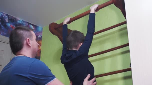 El padre enseña a su hijo a tirar hacia arriba en la barra horizontal en casa. practicar deportes con un niño adolescente. criar niños sanos. el cuidado de los niños — Vídeos de Stock