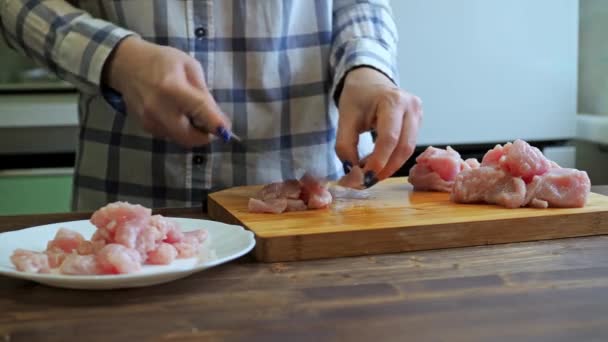 Uma mulher corta um filé de peru em uma tábua de madeira de corte. cozinhar na cozinha. close-up de mãos com uma faca e uma mesa — Vídeo de Stock