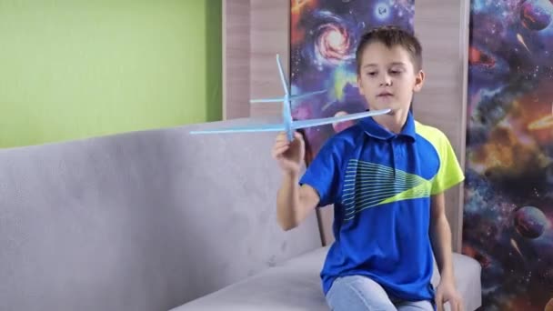 The boy is sitting on the couch playing with a blue airplane. the plane is made of foam. launches it forward at the camera. the plane flies into the lens — Video Stock