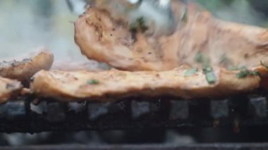 Izgarada tavuk filetosu pişirmek. Aşçı ızgaradaki fileto dilimlerini maşayla çevirir. Arka planda bir yangın yanıyor