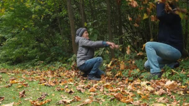 Father and son throw fallen leaves at each other. autumn fun in the park. golden autumn. family — Wideo stockowe