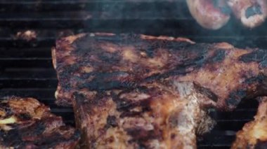 Domuz pirzolası ızgarada maşayla çevirilir. Kömürden çıkan duman. Izgarada yemek pişirmek. Yakın plan. kızarmış parça