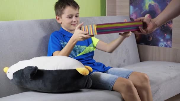 Opent de geschenkdoos. Verrassing en vreugde. Een man in een donker T-shirt zit op de bank. het kind presenteert een geschenk — Stockvideo