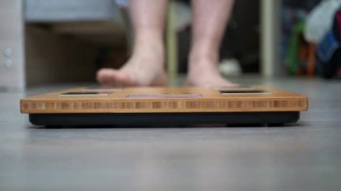 Erkeklerin kıllı bacakları terazide duruyor. Terazi burcu yakın planda. Aşırı kilolu olmanın sorunu