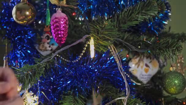 Közelkép a gyerekek kezét díszítő karácsonyfa egy szilveszteri labdát a háttérben fényes ünnepi fények. gyerekek díszítik a karácsonyfát — Stock videók