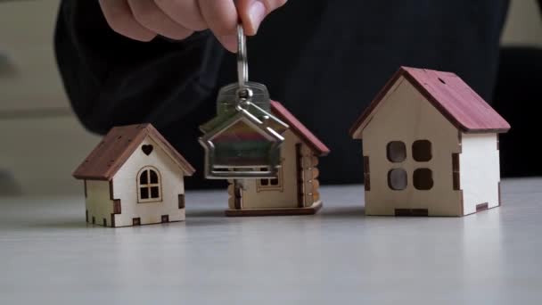 Kulcstartó lakáskulccsal a kezében. Játékházak az asztalon. ingatlan vásárlása. ingatlanügylet — Stock videók