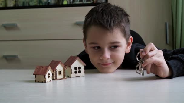 The child holds out a keychain with the keys to the new house. there are toy houses on the table.purchase of real estate. beautiful keys to the new building — стоковое видео