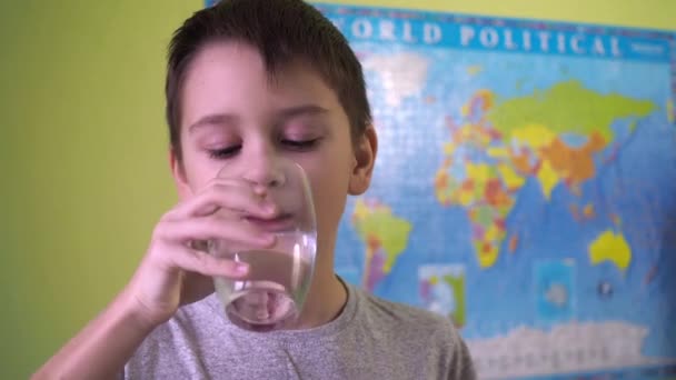 Un adolescent boit de l'eau dans un verre. puis il regarde la caméra et sourit. une carte politique du monde est suspendue sur le fond du mur — Video