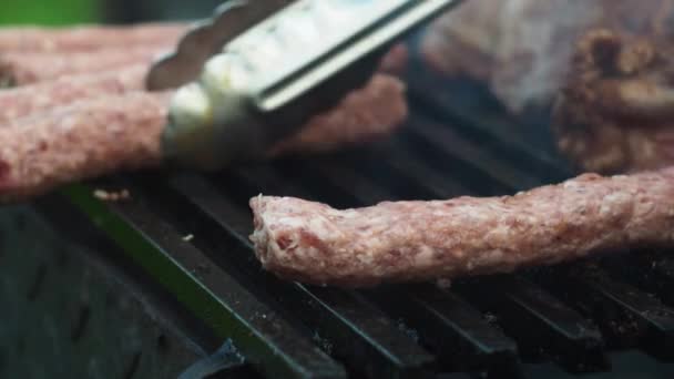 With tongs, he turns the sausages on the grill on the coals. the first ones are in focus, the rest are out of focus — Video
