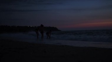 İnsanlar gün batımından sonra denizde yüzerler. Uzakta, insanlar denizde ve kıyıda görülebilir. Neşeli bir ruh hali. Güzel gökyüzü
