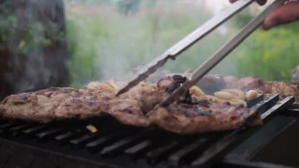 Cooking pork ribs on coals on the grill. a mans hand turns the ribs with tongs — Stock Video