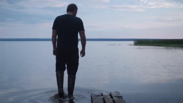 Muž vejde do jezera v botách a umyje si obličej. na cestu. klid jezera, měkké světlo zapadajícího slunce. turista — Stock video