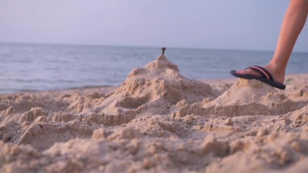 Ein Junge trampelt mit den Füßen auf einer Sandburg am Ufer des Meeres — Stockvideo