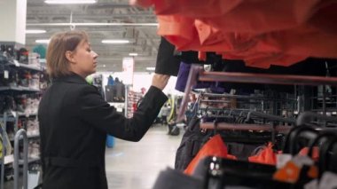 Mağazadaki bir kadın bir şeyler seçer. Askıda asılı eşofman üstü ve eşofman altı. spor mağazası