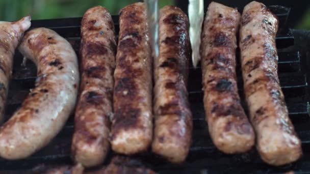 Sausages are grilled on coals cooking on a grill. turn it over with tongs. delicious food — Stock Video