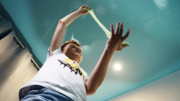 Un adolescent aruncă un slime pe cameră. luat de jos în sus. El fărâmițează jucăria de șopârle cu mâinile și o aruncă pe podea — Videoclip de stoc