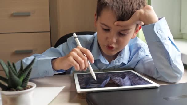Un estudiante dibuja en una tableta gráfica. un niño con una camisa azul aprende a dibujar sentado en una mesa — Vídeo de stock