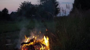 Bir adam eski gazeteleri, eski kıyafetleri, ağaç dallarını ateşe atar.