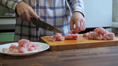 Bir kadın ahşap bir tahtanın üzerinde hindi filetosu kesiyor. Mutfakta yemek pişirmek. Bıçak ve masayla ellerinizi yakın çekin.