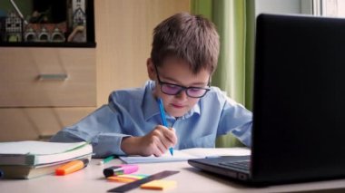 Uzaktan öğrenme. Genç bir öğrenci dizüstü bilgisayarda çalışıyor. Bir not defterine özet yazıyorum. Evde, yazı masasında oturuyor.