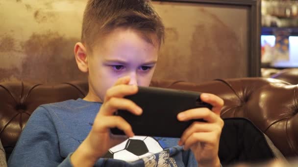 Egy tinédzser játszik a telefonban. a képernyő visszaverődése az arcon van. ül egy puha bőr kanapén, egy szobában meleg fény — Stock videók