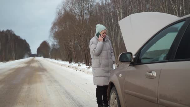 Uma mulher perto de um carro partido fora da cidade em uma estrada nevada. geada perigosa. situação de trânsito. chamar um reboque — Vídeo de Stock