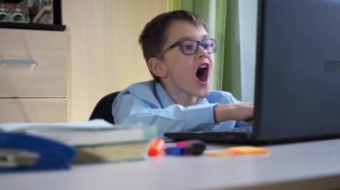 Uzaktan öğrenme. Gözlüklü bir öğrenci ağzını sürpriz bir şekilde açıyor. İnternette eğitim görüyor. yakın plan
