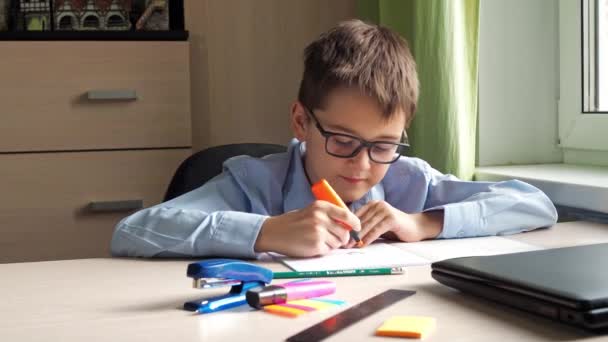 Een tiener in een blauw shirt tekent in een notitieboekje. schrijfmateriaal. een bureau. thuislessen — Stockvideo
