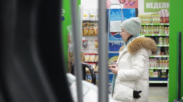 En kvinna i en järnaffär väljer varor med en telefon i handen. hon bär en vit rock med en vit hatt — Stockvideo