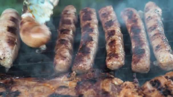 Kupaty gegrild op kolen koken op de grill. Draai het om met een tang. ongezond en vettig voedsel. rook van de grill. zijaanzicht — Stockvideo