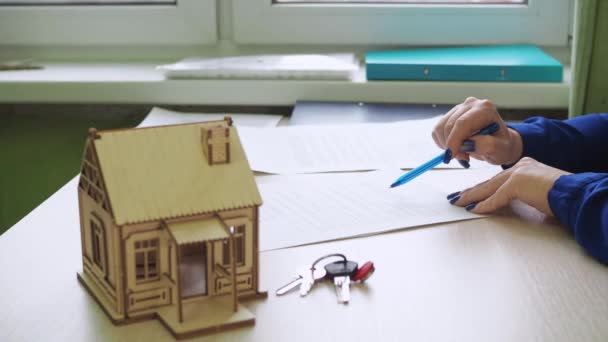 Женщина подписывает жилищный договор. покупка недвижимости. есть деревянный дом на столе, ключи от дома — стоковое видео