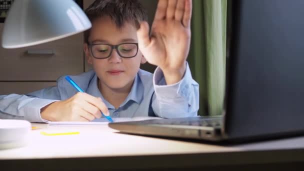 Genç bir öğrenci yazıyı kağıda yazıp kameraya gösterdikten sonra kameraya konuşuyor. Bilgisayarın ve ev derslerinin önünde masada oturmak. — Stok video
