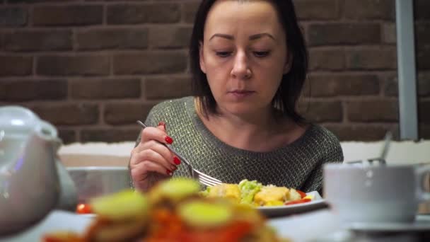 Uma rapariga num café à mesa a comer uma salada. morena bonito na mesa. césar com peixe — Vídeo de Stock